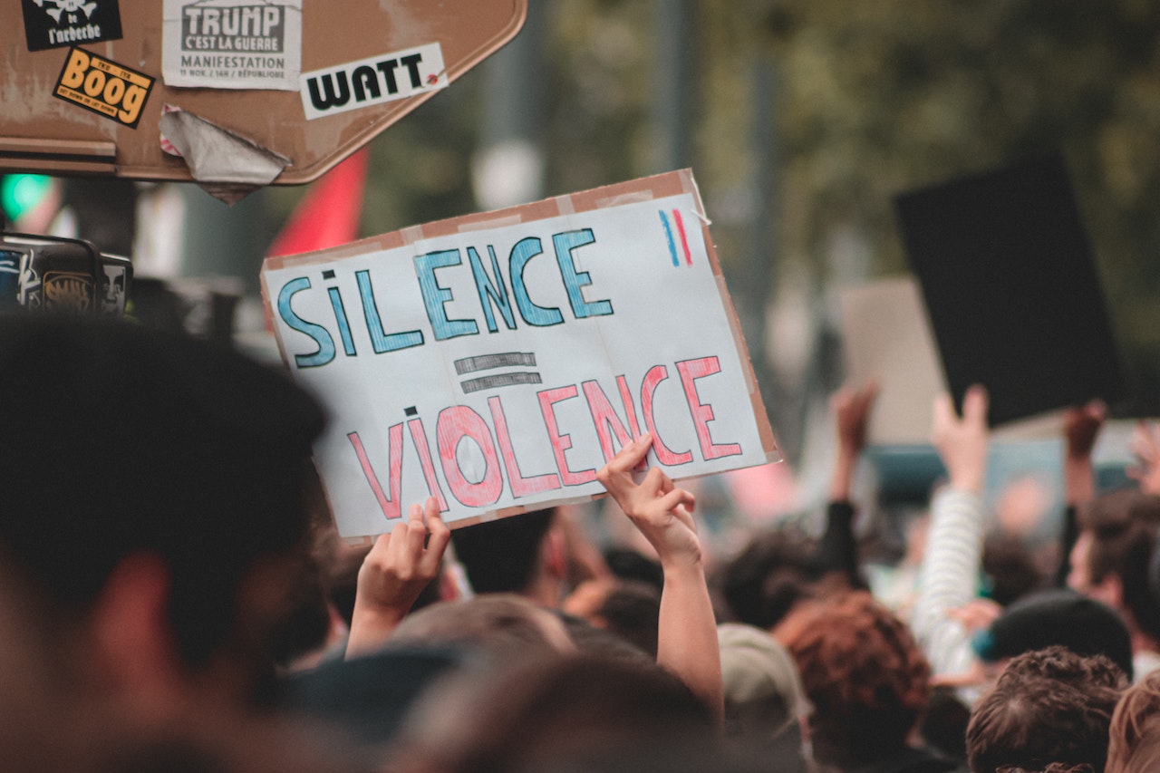 Faceless person in a rally holding a sign that has an equal sign between the words ‘silence’ and ‘violence’
