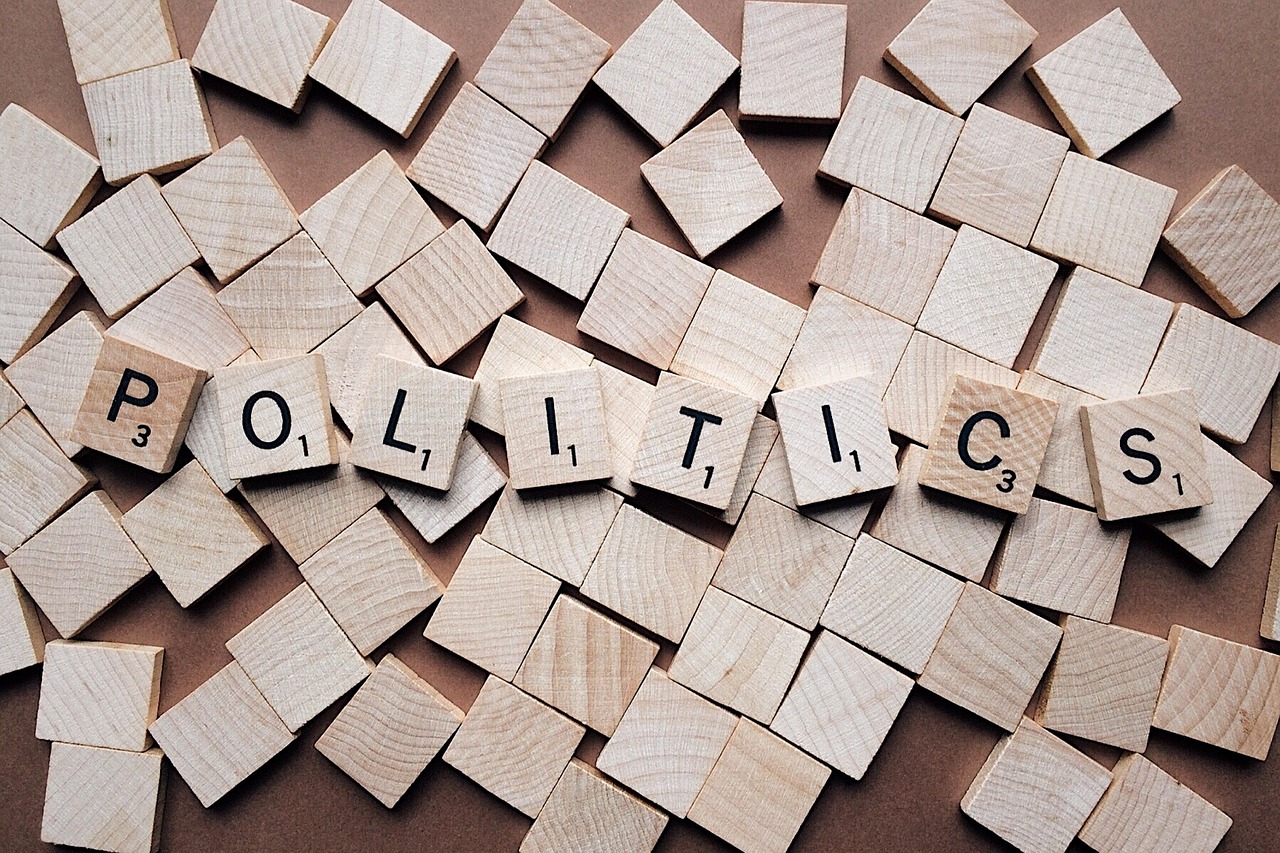 Wooden Scrabble letters facing down, with some on top of the others and forming the word, ‘politics’