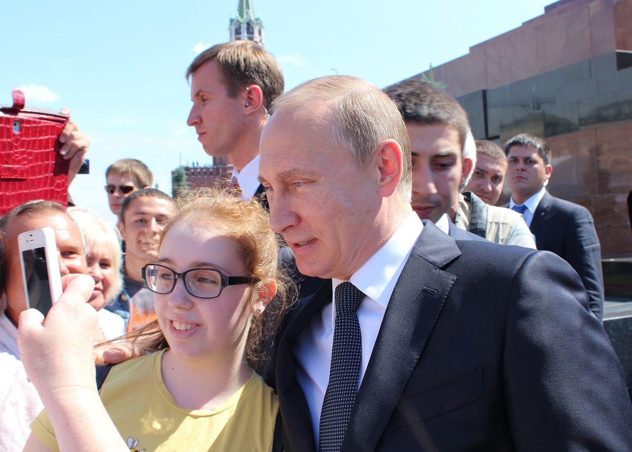 Vladimir Putin posing for a selfie with a young girl in public as male bodyguards watch over