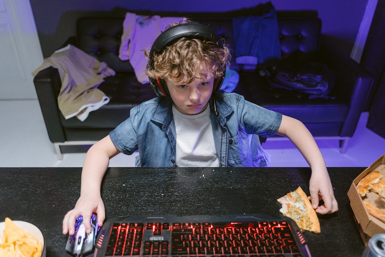 Boy in Blue Denim Jacket playing a video game with half eaten pizza