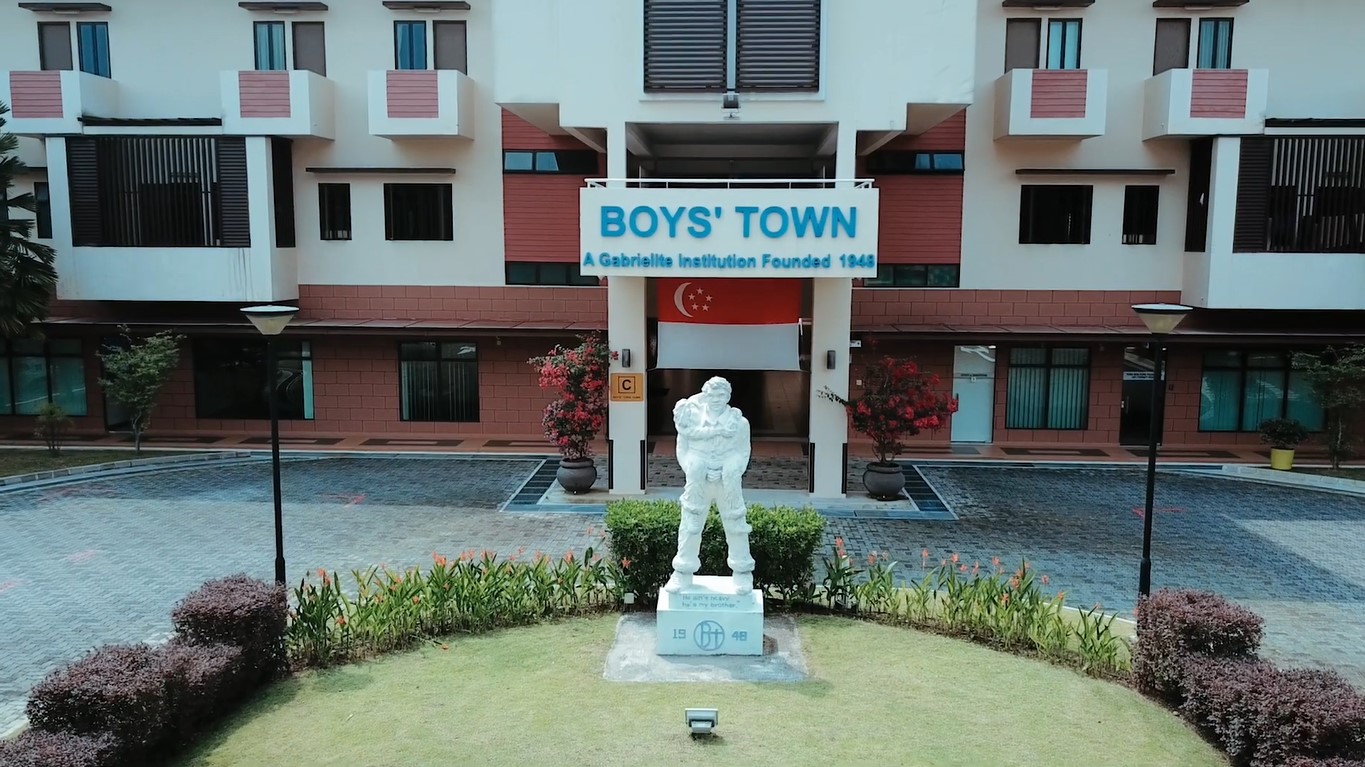 Façade of Boys’ Town in Singapore, with a statue painted in white of a man carrying a boy on his back