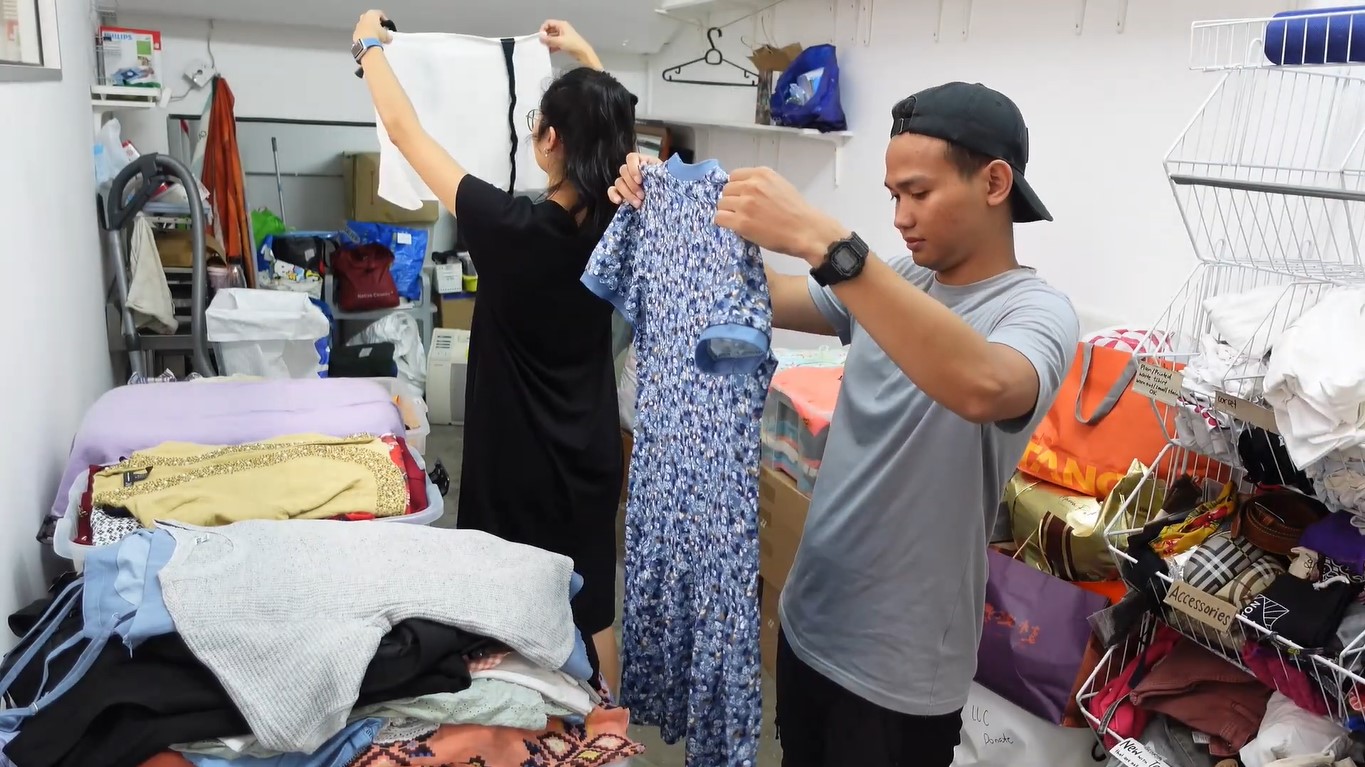 A young adult male and female Singaporean volunteers inside a Cloop storage room checking out donated clothes