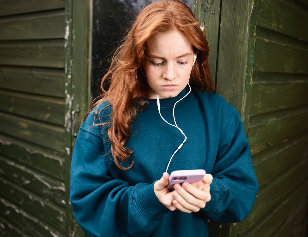 Redhead Woman Leaning against Wall Listening to Music from Phone