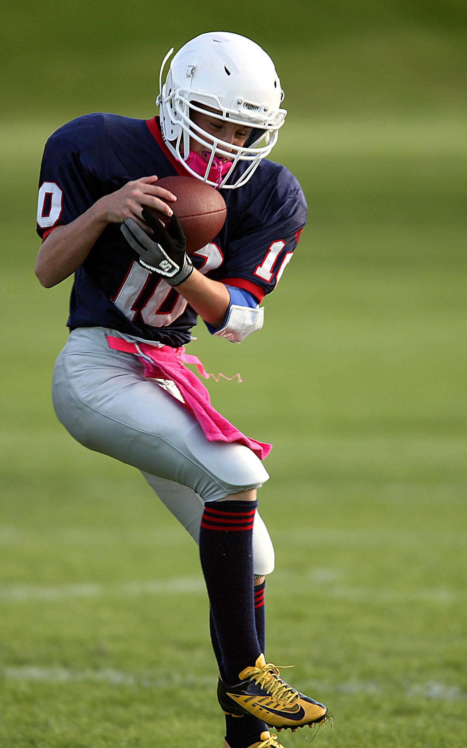 An American football player is holding ball in green grassy field.